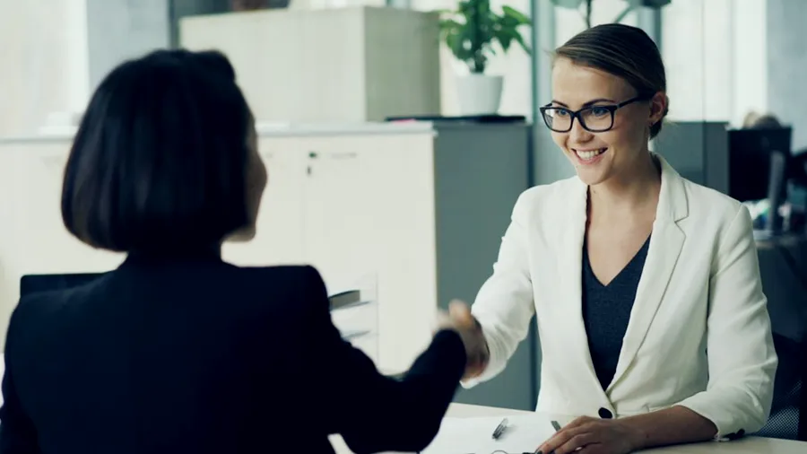 A recruiter and a candidate shaking hands in a Dubai office, standing for HR and payroll services